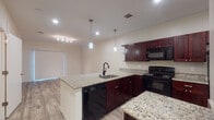 This single-floor residence showcases a thoughtfully designed open-concept layout where the kitchen flows seamlessly into the living area. The kitchen is a standout feature, equipped with rich dark cherry cabinetry, speckled granite countertops, and a full suite of black appliances, including an electric range, built-in microwave, refrigerator, and dishwasher. A peninsula with an undermount sink and elegant pendant lighting adds both functionality and style, while recessed lighting and a track light system ensure the space is well-illuminated throughout.

Wood-look plank flooring runs consistently through the living areas and bedrooms, creating visual continuity across the unit. The bedrooms are bright and comfortable, benefiting from large windows with blinds that allow natural light to filter in, complemented by ceiling fans for added comfort.

The bathrooms are finished to match the kitchen's aesthetic, featuring granite-topped dark vanities with undermount sinks, wood-look tile flooring, and ample storage. One bathroom includes a dedicated water closet and access to an additional room, adding a practical, well-organized feel to the space. Overall, the unit presents a clean, modern atmosphere with consistent, quality finishes throughout.