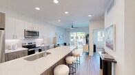 Located at 2058 East Apache Boulevard in Tempe, Arizona, this thoughtfully designed one-bedroom unit offers a modern, open-concept layout with stylish finishes throughout. The combined kitchen and living area serves as the heart of the space, where a large island with a quartz countertop and bar seating anchors the room. The kitchen is outfitted with stainless steel appliances, a subway tile backsplash, two-tone cabinetry featuring white upper cabinets and wood-finish lower cabinets, and recessed lighting overhead. Wood-style plank flooring extends throughout the main living areas, adding warmth to the clean, contemporary aesthetic. The living room benefits from abundant natural light and direct access to a private outdoor patio through sliding glass doors, while a ceiling fan adds comfort to the space. The generously sized bedroom features multiple windows fitted with horizontal blinds, a ceiling fan, and a serene, neutral palette that creates a restful atmosphere. A dedicated walk-in closet provides ample built-in shelving and hanging space to meet all storage needs. The unit's bright white walls, recessed lighting, and modern fixtures create a cohesive and polished look throughout.