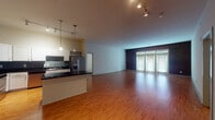 This single-floor residence offers a well-designed open-concept layout that seamlessly connects the kitchen and living areas. The kitchen is a standout feature, equipped with stainless steel appliances including a range, microwave, and refrigerator. White cabinetry with ample storage is complemented by dark granite countertops and a tiled backsplash. A central island with a matching dark granite surface provides additional prep space and casual seating. Pendant lighting and track lighting illuminate the kitchen, while hardwood-style flooring extends throughout the main living area.

The expansive living space is brightened by a large wall of French doors framed by an exposed brick accent wall, inviting natural light deep into the interior. Two bedrooms feature plush carpeting, ceiling fans, and windows with blinds. The bathrooms are finished with light tile flooring, white cabinetry, and tub-shower combinations. Additional carpeted spaces offer flexibility for use as a den or office. Track lighting throughout the main areas and neutral wall tones create a clean, functional atmosphere throughout the residence.