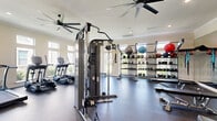Located at 1500 Highway 90 W in Sealy, Texas, this fitness center offers a comprehensively equipped workout facility designed to support a wide range of exercise routines. The single-floor gym is finished with durable rubber flooring throughout, providing a safe and functional surface for all types of training activity.

The cardio zone features multiple treadmills and elliptical machines positioned along a wall of large windows, flooding the area with natural light and offering pleasant outdoor views. Dual ceiling fans maintain comfortable airflow across the space. Crown molding and recessed lighting lend a polished, well-maintained aesthetic to the room.

The strength training area is equally well-appointed, housing a multi-function cable machine system alongside dedicated benches for pressing and functional movements. A full-length wall mirror expands the sense of space and supports proper form during workouts. An extensive free weight section includes multiple sets of dumbbells and kettlebells organized on tiered racks, along with an assortment of medicine balls and resistance bands for varied training options.

French doors connect the gym to an adjacent space, enhancing accessibility and the overall sense of openness. Wall-mounted artwork adds a touch of character to the environment. The facility is thoughtfully designed to accommodate both cardiovascular conditioning and comprehensive strength training in a bright, comfortable, and organized setting.