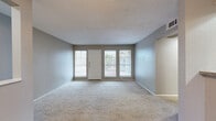 This well-organized single-floor unit offers a practical and comfortable layout across its thoughtfully arranged rooms. The living room serves as the heart of the space, featuring neutral-toned carpet flooring, textured walls painted in soft gray, and a textured ceiling. Large windows flanking the front entry door flood the area with abundant natural light and provide views of the surrounding exterior. A pass-through counter with a raised bar connects the living area to the kitchen, which is equipped with warm honey-toned wood cabinetry, dark appliances including a range and refrigerator, and a built-in overhead light fixture that brightens the compact cooking space. The bedroom is a quiet, carpeted retreat with a window offering natural light, and benefits from access to two closets, providing ample storage. The bathroom features a full tub-and-shower combination finished with classic white square tile, wood-look flooring, and a wall-mounted mirror above the vanity. Throughout the unit, consistent use of neutral gray tones and light carpet creates a cohesive, understated aesthetic. The layout is efficient and practical, making the most of the available footprint while maintaining a comfortable and livable atmosphere.