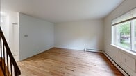 Located at 1238 Hartford Tpke in Vernon Rockville, CT, this multi-floor residence offers 2 bedrooms and 2 bathrooms spread across three levels, providing a well-organized and functional layout. The main living level features a spacious living room with warm hardwood flooring, neutral white walls, and baseboard heating throughout. Large windows allow natural light to flow in, offering views of the surrounding greenery and neighborhood.

The kitchen is equipped with warm oak cabinetry, light granite-style countertops, and white appliances including a range, dishwasher, and refrigerator. Tile flooring and a window overlooking the exterior complete the space. Both bedrooms feature the same hardwood flooring and neutral tones, with windows providing outdoor views. The primary bedroom offers a generous footprint with ample wall space.

The two bathrooms include one with classic white square tile wainscoting, a mirror cabinet, and baseboard heating, and a second with a pedestal sink, toilet, and tile flooring. A lower level provides a sizable open bonus area with a sealed concrete floor and exposed utility infrastructure, suitable for storage. Two staircases connect the floors throughout, adding accessibility and flow to this well-structured Vernon Rockville home.