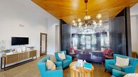 Located on McQueen Drive in Durham, NC, this single-floor community space offers a thoughtfully designed interior that balances function with contemporary style. The grand entrance greets visitors with soaring ceilings, an arched transom window, and floor-to-ceiling glass doors that flood the lobby with natural light. Elegant sheer drapery, teal upholstered seating, and a modern sputnik-style chandelier set a welcoming tone from the moment you step inside.

The open layout flows seamlessly into multiple lounge areas, each with its own distinct character. One section features a warm wood-paneled ceiling that creates an intimate atmosphere, complemented by vibrant turquoise armchairs and a textured glass accent wall. Another area showcases a coffered ceiling with recessed and pendant lighting, bold colorful artwork, and an eclectic mix of seating including woven accent chairs, red wingbacks, and a plush sectional — ideal for both casual gatherings and structured meetings.

Throughout the space, durable neutral-toned flooring ties the zones together, while carefully curated furnishings and accent pieces add pops of color and personality. Private rooms with glass-panel doors provide quieter breakout spaces, making this a highly versatile and inviting community hub in the heart of Durham.