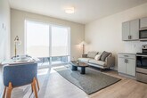 Located at 121 S Bristol St in Sun Prairie, Wisconsin, this efficiently designed one-bedroom unit makes smart use of its single-floor layout. The open-concept living and kitchen area anchors the space, bathed in natural light from large sliding glass doors that lead to an outdoor balcony. Light hardwood-style flooring runs throughout, complementing the neutral, warm-white walls that give the interior a clean, modern feel.

The kitchen is thoughtfully appointed with grey shaker-style cabinetry, white subway tile backsplash, light countertops, and a full suite of stainless steel appliances, including a range, over-the-range microwave, dishwasher, and refrigerator. The adjoining living area offers a welcoming atmosphere with generous natural light and direct balcony access.

The bedroom is a calm, well-organized retreat featuring built-in wall shelving, a closet, and direct access to an en-suite bathroom. The bathroom is finished with grey cabinetry, a dual-sink vanity, and a glass-door shower. A conveniently placed in-unit washer is tucked within a dedicated closet space in the bedroom, adding practical functionality. The overall aesthetic is modern and minimalist, making this a well-equipped and comfortable space.