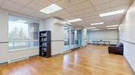 Located at 1241 Kilborn Place in Ottawa, Ontario, this single-floor multipurpose space offers a generously sized, open-concept layout designed for flexible use. The space is divided into two main areas, both finished with warm hardwood flooring and bright drop-tile ceilings equipped with recessed panel lighting throughout.

The primary open area is expansive and well-lit, featuring large windows along multiple walls that frame views of surrounding trees and outdoor greenery. A wall-mounted ductless mini-split air conditioning unit provides climate control, complemented by baseboard heating along the perimeter. Sliding glass patio doors connect the interior to an outdoor area, enhancing the sense of openness. A freestanding bookshelf adds a functional touch to this versatile area, which is currently configured to accommodate a full-size competition table tennis table. A seating nook with a leather sofa and coffee table creates a comfortable lounge corner, accessible through an interior doorway.

A separate entry vestibule features blue-framed glass doors, providing a welcoming and distinct point of access. The space also includes a dedicated kitchenette outfitted with white shaker-style cabinetry, subway tile backsplash, dark countertops, stainless steel appliances including a refrigerator, range, and over-the-range microwave, and a sink — all set on light-toned tile flooring. This well-appointed space is well-suited for community programming, recreation, or organizational use.