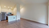 This single-floor residence features a thoughtfully designed open-concept layout, where the living area and kitchen flow seamlessly together. The living space is characterized by soaring vaulted ceilings, neutral white walls, and durable wood-style plank flooring that extends throughout the main areas, creating a bright and airy atmosphere. A sliding glass door opens onto a private balcony, framing pleasant views of surrounding greenery and allowing abundant natural light to fill the room.

The kitchen is well-appointed with stainless steel appliances, including a refrigerator, electric range, and built-in microwave. Two-tone cabinetry—white uppers and warm wood-toned lowers—pairs with a stone-look countertop peninsula and a subway tile backsplash, offering both functionality and visual interest.

The two bedrooms are carpeted for comfort, each featuring large windows with tree views and baseboard heating. The primary bedroom connects to a private bathroom with a walk-in shower and a wood-toned vanity. A second full bathroom includes a tub-shower combination. Conveniently, a stacked washer and dryer unit is housed within the unit, providing in-unit laundry access.