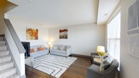This multi-story home spans three floors, offering a generous and versatile layout suited for comfortable everyday living. The living area immediately draws attention with its elevated ceiling that adds a sense of openness and volume to the space. Rich hardwood flooring runs throughout, providing warmth and continuity across the main level. Neutral-toned walls serve as a refined backdrop, complemented by tasteful décor including bold, colorful wall art that brings energy and personality to the room. The living space is thoughtfully arranged to accommodate both relaxed lounging and casual conversation, with ample room for multiple seating configurations. Natural light filters in through well-positioned windows, keeping the interior bright and inviting. The clean lines of the architecture are reflected in the smooth, angled ceiling detail, adding a subtle architectural interest to the overall design. The combination of modern finishes, warm tones, and carefully considered layout creates an ambiance that is both stylish and welcoming. With three full floors, this home provides significant flexibility for a variety of living arrangements, offering distinct spaces for entertaining, rest, and everyday activities across each level.