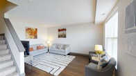 This multi-story home spans three floors, offering a generous and versatile layout suited for comfortable everyday living. The living area immediately draws attention with its elevated ceiling that adds a sense of openness and volume to the space. Rich hardwood flooring runs throughout, providing warmth and continuity across the main level. Neutral-toned walls serve as a refined backdrop, complemented by tasteful décor including bold, colorful wall art that brings energy and personality to the room. The living space is thoughtfully arranged to accommodate both relaxed lounging and casual conversation, with ample room for multiple seating configurations. Natural light filters in through well-positioned windows, keeping the interior bright and inviting. The clean lines of the architecture are reflected in the smooth, angled ceiling detail, adding a subtle architectural interest to the overall design. The combination of modern finishes, warm tones, and carefully considered layout creates an ambiance that is both stylish and welcoming. With three full floors, this home provides significant flexibility for a variety of living arrangements, offering distinct spaces for entertaining, rest, and everyday activities across each level.
