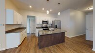 Located at 3862–3866 Buffalo Road in Rochester, NY, this single-floor residence offers a thoughtfully designed layout that balances functionality and modern style throughout. The kitchen serves as a central highlight, featuring white shaker cabinetry, granite countertops, and a full suite of stainless steel appliances, including a side-by-side refrigerator with ice and water dispenser, an electric range, and an over-the-range microwave. A substantial center island with a double sink and pendant lighting overhead provides both additional prep space and a natural gathering point. The kitchen flows seamlessly into the dining and living areas, where wood-look flooring extends throughout, a chandelier marks the dining space, and a ceiling fan with natural light from vertical-blind-covered sliding doors enhances the living area. A dedicated laundry room accommodates a full-size washer and dryer. The bedroom features plush carpeting, a large window with outdoor views, and direct access to a full bathroom and a generously sized walk-in closet outfitted with wire shelving on multiple walls. Neutral tones, clean white trim, and consistent finishes contribute to a cohesive and move-in-ready ambiance throughout the space.