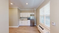 Located at 2400 NE 112th Ave in Vancouver, Washington, this efficiently designed single-floor studio unit offers a thoughtful layout that maximizes every square foot. The open-plan living, dining, and kitchen area is finished with warm beige walls, crisp white crown molding, and light wood-style vinyl plank flooring that lends a clean, contemporary feel throughout. Recessed lighting and multiple windows fitted with horizontal blinds allow natural light to filter into the space, creating a bright and welcoming atmosphere.

The kitchen is well-appointed with white shaker-style cabinetry, a mosaic tile backsplash, a smooth cooktop, built-in microwave, and a stainless steel refrigerator — providing all the essential appliances in a compact, functional footprint. A wall-mounted HVAC unit serves both the living and kitchen areas for year-round climate control.

A hallway with recessed lighting connects the main living space to the full bathroom, which is designed with accessibility in mind. The bathroom features warm-toned mosaic tile flooring, a wall-mounted sink with a granite-style countertop, and a roll-in shower with grab bars and a handheld showerhead, accented by natural wood-tone wall tiles. This unit is well-suited for those seeking a practical, move-in-ready space with modern finishes.