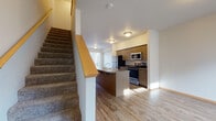 This two-story residence is designed with a practical, open layout that maximizes functionality across both levels. The main floor centers around a well-appointed kitchen featuring medium-toned wood cabinetry, granite-style countertops, and a full suite of stainless steel appliances, including a refrigerator, range, and built-in microwave. A peninsula with an integrated sink extends into the living area, creating a natural divide while maintaining an open-concept feel. The living space is finished with light hardwood-style flooring that runs throughout the main level, complemented by neutral walls and natural light from large windows. A carpeted staircase with a warm wood railing leads to the upper floor. The upper level features carpeted bedrooms with windows that bring in natural light; at least one bedroom includes a built-in closet. The bathrooms are finished consistently, each offering wood-tone vanity cabinetry topped with granite-style counters, an oval sink, and hardwood-style flooring. The overall aesthetic is clean and cohesive, with warm wood accents and neutral tones creating a welcoming, move-in-ready atmosphere throughout.