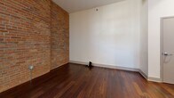 This 830 square foot apartment in Davenport, Iowa, offers a harmonious blend of modern amenities and industrial charm. The space features two bedrooms, including a primary bedroom of 130 square feet, and one bathroom. The open-concept living area is characterized by rich hardwood flooring that runs throughout, creating a warm and cohesive feel.

The kitchen is a highlight, boasting granite countertops, stainless steel appliances, and wooden cabinetry. A central island provides additional counter space and casual seating. Exposed wooden beams and pillars add rustic character, while exposed ductwork in the ceiling contributes to the industrial aesthetic.

One of the most striking features is the exposed brick wall, which adds texture and historical charm to the living space. Large windows allow for ample natural light, enhancing the apartment's spacious feel. The bathroom, while not shown in detail, appears to have modern fixtures and tiled flooring.

The apartment includes the convenience of in-unit laundry, with a washer and dryer neatly tucked away. A sliding barn door adds a touch of farmhouse chic to one of the rooms, likely a bedroom or closet.

The overall design aesthetic successfully marries contemporary finishes with industrial elements, creating a stylish and unique living environment. High ceilings and an open floor plan contribute to the sense of spaciousness in this compact yet well-designed apartment.