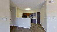 This single-floor residence offers a thoughtfully designed layout that balances functionality and comfort. The kitchen is a standout feature, showcasing rich dark-toned cabinetry with sleek hardware, white countertops, and a full suite of black appliances including a range, microwave, and refrigerator. A peninsula-style breakfast bar separates the kitchen from the adjacent living and dining areas, creating an open, connected feel that is ideal for everyday living and entertaining.

The dining area flows naturally from the kitchen and features warm wood-look flooring that extends throughout the main living spaces, complemented by a stylish pendant light fixture overhead. The spacious living room benefits from multiple windows that invite natural light and provide views of the surrounding greenery, with a ceiling fan adding to the room's comfort.

The bedroom is carpeted for warmth and comfort, featuring its own ceiling fan with lighting, a closet, and a window with blinds that allows for natural light. The bathroom is well-equipped with dark wood cabinetry, a vanity with a white countertop, a tub-shower combination, and wood-look flooring that ties into the overall design aesthetic. Neutral wall tones throughout the residence create a clean, cohesive backdrop ready for personalization.