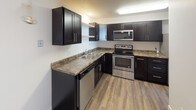 This single-floor, two-bedroom, one-bathroom unit offers a functional and straightforward layout. The living area features durable hardwood-style plank flooring in a warm, neutral tone, complemented by clean white walls and a natural wood-framed entry door. A large window with vertical blinds allows natural light to fill the space, while a baseboard heating unit ensures year-round comfort.

The kitchen is well-appointed with dark espresso cabinetry, granite-style countertops, and stainless steel appliances including an electric range, built-in microwave, and dishwasher. Light hardwood-style flooring ties the kitchen seamlessly to the main living area.

Both bedrooms feature soft carpeting, baseboard heating, and windows with blinds that provide natural light and privacy. One bedroom includes a closet with wooden doors, adding practical storage.

The full bathroom offers a clean, modern aesthetic with a dark vanity cabinet, white countertop, large mirror, and a full-size soaking tub with a shower surround. Neutral tile flooring and chrome hardware complete the space. Overall, the unit presents a simple, functional, and well-maintained living environment.