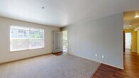This single-floor unit is designed with a practical, open layout that connects the main living areas cohesively. The living room serves as the central gathering space, featuring a combination of plush carpeting and wood-style hard flooring that defines distinct zones within the room. Neutral gray walls provide a clean, versatile backdrop, while a textured ceiling adds subtle visual interest. Natural light enters generously through a side window, and a glass-paneled door opens directly onto a private balcony, offering outdoor views of surrounding greenery.

The kitchen is situated adjacent to the living area and is equipped with light wood cabinetry, laminate countertops in a speckled gray finish, and a white electric range. The layout provides functional counter space on multiple sides, with overhead cabinets offering ample storage.

The bedroom is a well-proportioned space finished with carpeting and a large window that allows for abundant natural light. A door provides entry access to the unit from within this area.

The bathroom features wood-look vinyl flooring and includes a single-sink vanity with light wood cabinetry and a laminate countertop. A full bathtub and shower combination occupies a dedicated alcove, completing this functional and well-maintained space.