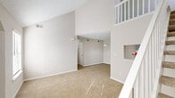 This two-story, three-bedroom unit in Virginia Beach, Virginia offers a well-designed layout with a clean, neutral aesthetic. The main level welcomes you with a carpeted living area featuring soaring vaulted ceilings and an open sightline to the upper floor, highlighted by a charming built-in display niche near the entry. A staircase with white balustrades connects both levels seamlessly. The galley-style kitchen is thoughtfully appointed with gray shaker cabinetry, white quartz countertops, a subway tile backsplash, stainless steel appliances including a range, microwave, and refrigerator, and light wood-style flooring. A dedicated laundry room with a full-size washer and dryer adds everyday convenience. The bedrooms are carpeted and spacious, with the upper-level rooms showcasing angled rooflines and vaulted ceilings that add architectural character. One upper bedroom benefits from a skylight that floods the space with natural light, along with a walk-in closet. Two full bathrooms serve the unit, each finished with gray vanity cabinetry, wood-style flooring, and a tub-shower combination. Throughout the unit, large windows invite ample natural light, and the consistent use of neutral tones creates a cohesive, move-in-ready environment.