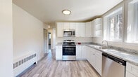 Located at 228 NY-376 in Hopewell Junction, NY, this single-floor, three-bedroom, one-bathroom home offers a clean, updated interior designed for comfortable everyday living. The kitchen serves as a standout feature, equipped with stainless steel appliances including a gas range with overhead microwave, dishwasher, and refrigerator. White shaker-style cabinetry with granite-look countertops and an undermount sink complete the space, while light hardwood-style flooring and large windows invite natural light and views of the surrounding greenery. A convenient exterior door in the kitchen provides direct outdoor access. The living room continues the hardwood-style flooring and is outfitted with a wall-mounted air conditioning unit and baseboard heating, ensuring year-round comfort. Each of the three bedrooms features plush carpeting, natural light from sliding or double-pane windows, and ample closet space — with four closets distributed throughout the home. The primary bedroom offers generous proportions and a sliding-door closet. The full bathroom is neatly appointed with a tiled tub-shower combo, a white vanity, and hardwood-style flooring, maintaining the home's consistent, clean aesthetic throughout.