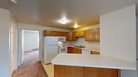 Located at 5801 Copper Beech Blvd in Kalamazoo, Michigan, this single-floor unit offers a straightforward and functional layout designed for everyday living. The kitchen serves as a central feature, equipped with warm oak cabinetry providing ample upper and lower storage, white appliances including a refrigerator, electric range, built-in microwave, and dishwasher, along with light-toned countertops and a double-basin sink. A peninsula extends from the kitchen, creating a natural division between the cooking area and the adjacent living space while offering additional counter space. The flooring in the kitchen transitions between tile and carpet as rooms shift throughout the unit. The living area is carpeted and receives natural light through a window with exterior views of surrounding greenery. A wall-mounted air conditioning unit and baseboard heating provide climate control throughout. The bedrooms are carpeted and neutrally finished, each featuring windows that admit natural light. One room provides direct access to an in-unit laundry area. The bathroom includes a single-sink oak vanity with a white countertop, a tub and shower combination, a large mirror, and tile flooring. Throughout the unit, the neutral color palette and consistent use of oak millwork contribute to a cohesive, practical aesthetic.