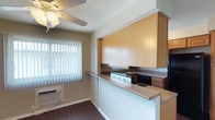 This single-floor residence offers a practical and functional layout designed for comfortable everyday living. The living area is finished with rich, dark hardwood-style flooring that extends throughout the main spaces, complemented by neutral-toned walls and a ceiling fan that enhances air circulation and light. Vertical blinds on the windows allow for adjustable natural light throughout the day, and a wall-mounted HVAC unit provides climate control.

The kitchen is well-appointed with warm wood cabinetry offering generous storage, a double-basin sink, coil-burner electric range, over-the-range microwave, dishwasher, and a full-size refrigerator — all finished in black. Countertops provide ample workspace, and a window above the sink brings in natural light. A secondary kitchen area features a peninsula-style counter with additional upper cabinetry, ideal for casual dining or food prep.

The bedrooms are carpeted for warmth and comfort, featuring neutral walls and multiple windows dressed with vertical blinds that fill the rooms with natural light. Sliding panel closets with built-in hanging rods and shelving provide practical storage solutions.

The bathroom is clean and functional, featuring a soaking tub with a showerhead, warm-toned tile surround, and a small window for ventilation and natural light.