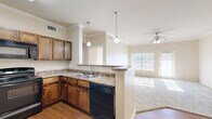 This thoughtfully designed 1-bedroom, 1-bathroom residence offers an efficient and comfortable single-floor layout. The heart of the home is an open-concept living, dining, and kitchen area, where warm hardwood-style flooring flows seamlessly throughout. The kitchen is equipped with rich dark wood cabinetry, stone-look countertops, black appliances including a range, dishwasher, and microwave, and a peninsula with pendant lighting that serves as both a workspace and casual dining area. Crown molding adds a refined architectural detail throughout the common areas.

The living room is carpeted and bathed in natural light from large windows with blinds, and is further enhanced by a ceiling fan. The bedroom is a comfortable, well-sized retreat featuring plush carpeting, a ceiling fan, a window for natural light, and direct access to a dedicated closet. The unit also includes three closets in total, a pantry, and an in-unit laundry space, providing excellent storage and convenience.

The full bathroom features large-format tile flooring, a dark wood vanity with stone-look countertop, a full soaking tub with shower, and clean, neutral finishes throughout. The overall ambiance is warm and functional, with a neutral color palette that lends itself well to personalization.