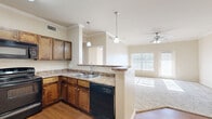 This thoughtfully designed 1-bedroom, 1-bathroom residence offers an efficient and comfortable single-floor layout. The heart of the home is an open-concept living, dining, and kitchen area, where warm hardwood-style flooring flows seamlessly throughout. The kitchen is equipped with rich dark wood cabinetry, stone-look countertops, black appliances including a range, dishwasher, and microwave, and a peninsula with pendant lighting that serves as both a workspace and casual dining area. Crown molding adds a refined architectural detail throughout the common areas.

The living room is carpeted and bathed in natural light from large windows with blinds, and is further enhanced by a ceiling fan. The bedroom is a comfortable, well-sized retreat featuring plush carpeting, a ceiling fan, a window for natural light, and direct access to a dedicated closet. The unit also includes three closets in total, a pantry, and an in-unit laundry space, providing excellent storage and convenience.

The full bathroom features large-format tile flooring, a dark wood vanity with stone-look countertop, a full soaking tub with shower, and clean, neutral finishes throughout. The overall ambiance is warm and functional, with a neutral color palette that lends itself well to personalization.
