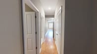This efficiently laid-out 2-bedroom, 1-bathroom unit offers a clean, modern aesthetic throughout. Warm hardwood-style flooring runs continuously across the entire space, complemented by neutral gray walls and crisp white trim, creating a cohesive and inviting atmosphere.

A long, well-lit hallway connects the key areas of the unit, lined with white panel doors and recessed lighting overhead. The galley-style kitchen features white shaker cabinetry, gray countertops, a stainless steel sink, and stainless steel appliances, including a refrigerator, range, and microwave — all arranged efficiently along one wall.

Both bedrooms are thoughtfully sized, with the primary bedroom offering ample space, a ceiling fan with a light fixture, and a well-organized closet with wire shelving. The second bedroom mirrors the same neutral finishes and ceiling fan setup, providing a comfortable and versatile space.

The bathroom is a standout feature, showcasing marble-look tile flooring, a dual-sink vanity with gray cabinetry, a large wall mirror, and a full tub-shower combination with elegant blue mosaic tile accents. The overall design is clean and contemporary, making this a functional and attractive living space.