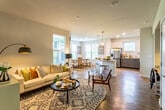 This thoughtfully designed single-floor residence offers a seamless blend of modern finishes and comfortable living. A welcoming hallway with warm hardwood-style flooring and a decorative mirror sets the tone as you move through the home. The living room is a bright, inviting retreat featuring large windows that draw in natural light, neutral walls, and hardwood-style floors. The kitchen is a standout, showcasing two-tone cabinetry with crisp white uppers and slate-gray lowers, granite countertops, stainless steel appliances, a tile backsplash, and an island with a sink — all flowing effortlessly toward an adjacent dining area. The sun-filled dining space is framed by multiple windows overlooking a green outdoor view, offering a relaxed setting for meals. The primary bedroom is generously proportioned with ample natural light and connects to a well-appointed en-suite bathroom complete with a double vanity featuring granite counters and navy cabinetry, a soaking tub, and a separate glass-enclosed shower with tile surround. A spacious walk-in closet with built-in shelving provides excellent storage. An additional bedroom with carpet flooring, natural light, and a ceiling fan rounds out this comfortable and cohesive home.