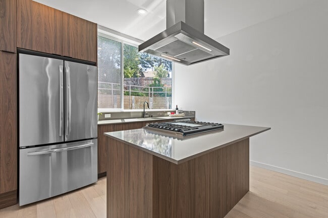 Estufa a gas con campana extractora y refrigerador con puertas francesas más allá. - 6026 Sand Point Way NE