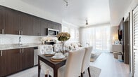 This thoughtfully designed single-floor residence blends modern aesthetics with functional living. The open-concept layout seamlessly connects the kitchen, dining, and living areas, creating a cohesive and welcoming environment throughout.

The kitchen is outfitted with rich dark wood cabinetry, granite countertops, a classic subway tile backsplash, and a full suite of stainless steel appliances, including a refrigerator, range, microwave, and dishwasher. A dining area sits adjacent to the kitchen, offering an intimate setting for everyday meals.

The living room is a bright, airy retreat, highlighted by a paneled accent wall, a ceiling fan, and floor-to-ceiling sliding glass doors dressed in sheer white curtains that open to an outdoor balcony. A striking vertical wood slat feature wall anchors the entertainment area, adding warmth and texture to the otherwise light, neutral palette.

The bedroom is a calm and comfortable space, bathed in natural light from a large window. Light hardwood-style flooring runs throughout, contributing to the home's clean, contemporary feel.

The full bathroom features large-format tile flooring, a soaking tub with shower, dark wood vanity with granite countertop, and a wide mirror, maintaining the refined design language found across the entire residence.