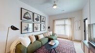 This single-floor residence offers a thoughtfully designed layout with a cohesive contemporary aesthetic throughout. The living room serves as the heart of the home, featuring a ceiling fan, a large window dressed with sheer curtains that invite natural light, and a striking gallery wall showcasing six geometric art pieces. A plush green sectional sofa, patterned area rug, and oval coffee table complete the welcoming atmosphere.

The kitchen is outfitted with white shaker-style cabinetry, white quartz countertops, a subway tile backsplash, and stainless steel appliances including a refrigerator, range, and over-the-range microwave. Light wood-look flooring ties the space together, while a peninsula island with bar seating provides casual dining and additional workspace. Recessed lighting and high ceilings in this area enhance the open, airy feel.

The primary bedroom features plush carpeting, a ceiling fan, and a bold burgundy upholstered bed frame accented by warm wood nightstands and a woven wall hanging. A second bedroom offers equally comfortable accommodations with a dark-toned dresser, framed wall art, and natural light from a large window.

The bathroom is finished with wood-look flooring, a single-sink vanity with white cabinetry, and a glass-enclosed walk-in shower tiled in classic white subway tile, offering a clean and functional design.