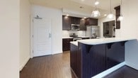 This single-floor, two-bedroom, two-bathroom residence offers a thoughtfully designed layout with a cohesive blend of modern finishes and functional living spaces. The kitchen serves as a standout feature, showcasing rich dark cabinetry paired with light marble-style countertops, a subway tile backsplash, and a full suite of stainless steel appliances including a range, microwave, refrigerator, and dishwasher. A dark-paneled kitchen island with pendant lighting overhead adds both style and additional workspace. Tucked conveniently off the kitchen is an in-unit laundry closet housing a stacked washer and dryer. Hardwood-style flooring runs throughout the main living areas, while the open living and dining space is finished with crown molding, ceiling fans, and natural light from a large window. Both bedrooms are carpeted and generously sized, each offering built-in closets and a calm, neutral palette. The bathrooms are finished in clean white tile with a soaking tub and shower combo, brushed nickel fixtures, and tile flooring, providing a bright and functional design.