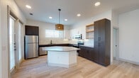 Located at 325 Melba St in Dallas's 75208 zip code, this single-story home showcases a contemporary design with a clean, modern aesthetic carried consistently throughout. Light wood-toned flooring flows seamlessly across the open-concept living and kitchen areas, enhancing the sense of continuity and space.

The kitchen serves as a central highlight, featuring a two-tone cabinetry scheme that pairs crisp white upper cabinets with rich dark lower cabinets. A marble-style tile backsplash adds elegance, while open wood shelving introduces a warm, organic contrast. A central island with a quartz-style countertop anchors the space beneath a distinctive woven pendant light fixture. Stainless steel appliances, including a refrigerator, range, and microwave, complete the functional design. French doors and multiple windows bring in abundant natural light.

The bathrooms reflect the same attention to detail. One features a tub-shower combination with large-format marble-look tile and matte black hardware. The primary bath includes a walk-in shower with built-in shelving, a wood-toned vanity, decorative pendant lighting, a herringbone accent wall, and direct access to a walk-in closet. Additional rooms are bright and versatile, with recessed lighting and generous window placement.