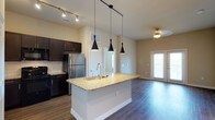 This 2-bedroom, 2-bathroom residence is laid out on a single floor, offering a functional and stylish living experience. The open-concept kitchen and living area serves as the heart of the home, featuring rich dark-espresso cabinetry, stainless steel appliances, and a classic white subway tile backsplash. A central kitchen island with a granite countertop and an undermount sink adds both prep space and a natural gathering point. Three sleek pendant lights hang above the island, providing focused task lighting with a contemporary flair, while track lighting enhances the kitchen further. Durable hardwood-style flooring runs throughout the main living area, adding warmth and cohesion. The adjoining living space is generously proportioned, bathed in natural light from a large window, and finished with a ceiling fan for year-round comfort. Neutral wall tones throughout create a bright and welcoming ambiance, offering a versatile backdrop for any décor style. The layout flows intuitively, with clear sightlines connecting the kitchen to the living area and access points leading to the bedrooms and bathrooms beyond.