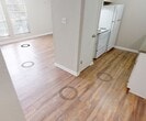 This two-story townhouse in Lafayette, Louisiana offers a practical and comfortable layout across two levels. The main floor features hardwood-style flooring throughout the living and dining areas, which are bathed in natural light from large windows fitted with blinds. Ceiling fans with integrated light fixtures are present in the main living spaces, providing both airflow and illumination. A staircase with a wood railing connects the two floors, contributing to the townhouse's multi-level character. The kitchen is efficiently designed with white cabinetry, a double stainless steel sink, green-toned countertops, and hardwood-style flooring, providing ample storage and workspace. The bedroom, located on the upper level, is carpeted for comfort and features large windows that invite generous natural light. A built-in open closet with shelving offers convenient storage. The bathroom includes a clean, white tub and shower unit alongside standard fixtures. Neutral warm-beige tones on the walls throughout the home create a cohesive, understated aesthetic. Textured ceilings add a subtle architectural detail consistent across the space. This townhouse provides a straightforward, functional living environment well-suited for those seeking a compact yet complete two-story home in Lafayette.