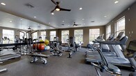 This fitness center offers a comprehensive workout environment designed to accommodate a wide range of exercise needs. The single-level space features a durable, dark speckled flooring suitable for high-traffic athletic use, while recessed lighting and dual ceiling fans ensure the room remains well-lit and comfortably ventilated throughout.

A full wall of mirrors lines one side of the room, enhancing the sense of space and allowing users to monitor their form during exercise. Large windows along the exterior wall allow ample natural light to fill the room, creating an open and energizing atmosphere with views to the outdoors.

The cardio section is equipped with multiple treadmills and stair climbers, positioned to take advantage of the natural light from the windows. The strength training area features a cable machine and weight bench, complemented by a colorful collection of stability and medicine balls. The layout is thoughtfully organized, providing clear zones for both cardio and resistance training without feeling crowded, making it a functional and inviting space for fitness enthusiasts of all levels.