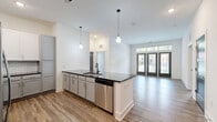 Located at 1900 Olevia St in Jacksonville, FL, this well-appointed 2-bedroom, 2-bathroom unit is spread across a single floor, offering a thoughtfully designed layout with modern finishes throughout. Wood-look plank flooring runs seamlessly through the open living areas, creating a cohesive and contemporary feel.

The open-concept kitchen is a standout feature, boasting two-toned cabinetry with white upper cabinets and gray lower cabinets, a white subway tile backsplash, dark stone countertops, a breakfast bar peninsula with pendant lighting, and stainless steel appliances. The adjacent living area is bright and airy, with tall ceilings, large French doors topped with transom windows, and ample natural light.

Both bedrooms are well-sized, with the primary bedroom offering a ceiling fan and generous windows with outdoor views. Each bedroom is served by its own dedicated walk-in closet fitted with multi-level wire shelving systems for organized storage.

The bathrooms are elegantly finished, featuring gray vanity cabinetry with granite countertops, black matte fixtures, and white subway tile surrounds. The primary bath includes a glass-enclosed walk-in shower, while the secondary bath offers a full soaking tub and shower combination. Clean white walls and elevated ceiling heights enhance the sense of openness throughout the entire space.