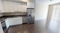 This single-floor unit offers a clean, contemporary design throughout. The open-concept living area flows seamlessly from the kitchen, anchored by rich, dark hardwood flooring that adds warmth to the neutral, light-toned walls. The kitchen is well-equipped and thoughtfully laid out, featuring sleek white cabinetry with modern hardware, dark granite-style countertops, and a full suite of stainless steel appliances including a side-by-side refrigerator with ice and water dispenser, a gas range, an over-the-range microwave, and a dishwasher. A stainless steel sink with a modern faucet completes the functional workspace. The spacious living area adjacent to the kitchen offers an open, airy feel with recessed lighting overhead. The bedroom is finished with plush wall-to-wall carpeting, neutral warm-toned walls, and a window fitted with horizontal blinds that allows natural light to filter in. The full bathroom features a white vanity with dark granite countertops, an undermount sink with brushed nickel fixtures, a large mirror, and a full bathtub and shower combination. The overall ambiance of the space is modern, clean, and move-in ready.