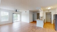 This well-appointed single-floor residence offers a clean, contemporary design throughout, highlighted by light hardwood flooring, crisp white walls, and a textured ceiling that runs seamlessly across the open-concept main living area. The spacious living room is bathed in natural light through a large sliding glass door that opens onto a private balcony overlooking lush greenery, and is equipped with a ceiling fan for year-round comfort. The kitchen is thoughtfully designed with white shaker-style cabinetry, quartz countertops, a classic subway tile backsplash, stainless steel appliances, and a peninsula featuring a black matte faucet and undermount sink — ideal for both cooking and casual dining. A dedicated pantry with built-in shelving provides ample storage. The two bedrooms are well-sized, each featuring hardwood floors, neutral tones, and windows with blinds that invite natural light. Both bathrooms are finished to a high standard, showcasing white cabinetry, quartz vanity tops, illuminated LED mirrors, black matte hardware, and a tub-shower combination with white tile surround. A dedicated laundry area accommodates a full-size washer and dryer, adding everyday convenience to this thoughtfully designed home.