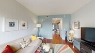 Located at 221 Cherry St S in Winston-Salem, NC, this single-floor residence offers a thoughtfully designed layout with a seamless flow between living, sleeping, and kitchen spaces. Rich hardwood flooring runs throughout, anchoring the home with warmth and continuity.

The living area is bright and welcoming, featuring soft neutral walls accented by a cool blue feature wall, and a sliding glass door that opens to a private balcony, filling the room with natural light and offering outdoor views. The open arrangement comfortably accommodates a full seating area and makes an ideal space for relaxing or entertaining.

The kitchen is well-appointed with crisp white cabinetry extending to the ceiling for ample storage, granite-style countertops, a double stainless steel sink, and a full suite of stainless steel appliances including a range, microwave, and dishwasher. The clean, functional design makes it both practical and visually appealing.

The bedroom is generously proportioned with its own sliding glass door leading to the balcony, allowing for natural light and outdoor access. The light-toned walls and hardwood floors carry throughout, maintaining a cohesive aesthetic.

The bathroom features tile flooring, a modern vanity with frosted glass cabinet details, a large mirror, and bright overhead lighting, completing this well-rounded residence.