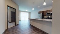 Located at 7600 Terrace Ave in Middleton, Wisconsin, this single-floor unit offers a well-designed open-concept layout that connects the kitchen and living area seamlessly. The kitchen is a standout feature, equipped with rich dark-toned cabinetry, granite countertops, stainless steel appliances including a refrigerator, stove, and microwave, and a peninsula with pendant lighting overhead. Wood-look hard flooring extends throughout the main living areas, adding warmth and cohesion to the space. A large sliding glass door with vertical blinds floods the living area with natural light and provides access to an outdoor area. The bedroom is generously sized with plush carpeting, dual windows with blinds allowing ample daylight, and a modern door with sleek hardware. The bathroom features granite countertops, dark cabinetry, wood-look flooring, and a full shower-tub combination. A dedicated in-unit laundry area accommodates a stacked washer and dryer, adding everyday convenience. Neutral wall tones and consistent contemporary finishes throughout create a clean, cohesive aesthetic suited for comfortable, modern living in the Middleton community.