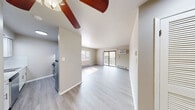 This single-floor residence offers a clean, functional layout with consistent light-toned luxury vinyl plank flooring throughout. The open living area is a standout feature, offering generous room to move and natural light streaming in from multiple windows. A ceiling fan provides year-round comfort, while a wall-mounted air conditioning unit and baseboard heating ensure climate control in all seasons. Sliding glass doors open directly to a private balcony, offering pleasant outdoor views of surrounding greenery. The kitchen is well-appointed with crisp white shaker-style cabinetry, granite countertops with subtle grey and white veining, a classic subway tile backsplash, and stainless steel appliances including an electric range and refrigerator. An overhead range hood completes the cooking space efficiently. The bedroom is a quiet, comfortable retreat with a large window that invites natural light and connects to views of the outdoors, along with baseboard heating for warmth. The bathroom features a full tub-shower combination with brushed nickel fixtures and a curtain rod, paired with a standard toilet. Neutral warm-grey walls throughout the unit create a cohesive, move-in-ready aesthetic that is both practical and welcoming.