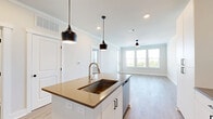Located at 210 Hills Rd in Panama City Beach, FL, this well-appointed 1-bedroom, 1-bathroom unit offers a thoughtfully designed single-floor layout with a clean, modern aesthetic. Light wood-tone flooring flows seamlessly throughout every room, complemented by crisp white walls, crown molding, and white baseboards that create a cohesive and airy atmosphere.

The open-concept kitchen and living area serves as the heart of the unit. The kitchen is outfitted with floor-to-ceiling white shaker-style cabinetry, dark hardware, a full suite of stainless steel appliances including a range, microwave, and refrigerator, and a central island with a dark quartz countertop and pendant lighting overhead—ideal for both cooking and casual dining.

The living area benefits from a glass exterior door and large windows with horizontal blinds, inviting ample natural light and outdoor views. A ceiling fan adds both function and style to this comfortable space.

The bedroom is generously sized, featuring dual windows that frame pleasant outdoor scenery and provide excellent natural light. The walk-in closet is equipped with multi-tier wire shelving for practical storage.

The bathroom is finished with white cabinetry, dark quartz countertops, black hardware accents, a tub-shower combination with tile surround, and direct access to the walk-in closet.