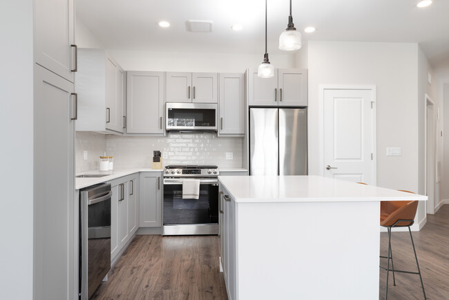 Modern kitchen with stainless steel appliances, white quartz countertop, light grey cabinetry, white tile backsplash, and hard surface flooring - Avalon Amityville