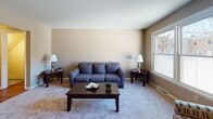 This three-floor residential property offers a well-organized and functional layout spread across its levels. The main living area is bright and welcoming, featuring neutral warm-toned walls, soft carpeting, and large windows that invite ample natural light while offering views of the surrounding neighborhood. The galley-style kitchen is efficiently designed with warm wood cabinetry, white countertops, and white appliances including a range and refrigerator, providing practical storage and workspace. Multiple bedrooms are found throughout the upper floors, each carpeted and finished with neutral taupe walls. The bedrooms are generously sized, featuring large windows with outdoor views and closets with bifold doors for storage. The primary bedroom is particularly spacious and well-appointed. The full bathroom includes a classic tiled tub-and-shower combination with chrome fixtures. A staircase connects all three floors, with the lowest level consisting of an unfinished basement that features concrete block walls, exposed ceiling joists, and utility infrastructure, offering significant potential for customization or additional storage. Throughout the home, the consistent neutral color palette and carpeted floors create a cohesive, comfortable atmosphere.