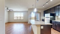 This single-story, 1-bedroom, 1-bathroom residence offers a thoughtfully designed layout that maximizes functionality and comfort. The open-concept kitchen and living area forms the heart of the home, featuring rich dark cabinetry, granite-style countertops, a center island with a sink, stainless steel appliances, and a classic subway tile backsplash. Pendant lighting and track lighting illuminate the space, while wood-style flooring runs throughout, adding warmth. Natural light flows in through multiple windows fitted with blinds, and a set of French doors provides access to an outdoor area. The living room is spacious and bright, with a ceiling fan overhead. The bedroom is carpeted for comfort, includes a ceiling fan and window with natural light, and connects directly to a generously sized walk-in closet outfitted with wire shelving. The full bathroom features a dark vanity with granite-style countertop, a tub-shower combination with tile surround, and brushed nickel fixtures. A dedicated laundry room houses a full-size washer and dryer set on wood-style flooring. The hallway connects all rooms efficiently, completing this practical and comfortable single-level layout.