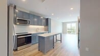 This 650 square foot apartment at 140 Valley Green Ln offers a thoughtful blend of style and functionality. The single-floor layout comprises one bedroom, one bathroom, and an open-concept kitchen and living area. The primary bedroom, measuring 130 square feet, provides ample space and is complemented by a closet for storage.

The kitchen is a standout feature, boasting sleek blue cabinetry, stainless steel appliances, and under-cabinet lighting that illuminates the white backsplash. A central island adds extra counter space and casual seating. The living area flows seamlessly from the kitchen, creating an ideal space for entertaining or relaxing.

Throughout the apartment, warm wood-tone flooring adds a touch of elegance and continuity. Large windows in the bedroom and living area flood the space with natural light, while also offering views of the surrounding area. The bathroom continues the modern aesthetic with a vanity that matches the kitchen's blue theme.

A notable feature is the in-unit laundry, visible in one of the images, adding convenience to daily life. The apartment's neutral wall colors provide a blank canvas for personal decor choices. Overall, this apartment offers a contemporary living experience in a well-designed, compact space.