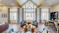 Located at 1150 E IH-20 in Grand Prairie, Texas, this single-floor communal space is thoughtfully designed to offer a welcoming and versatile gathering environment. The layout flows seamlessly across multiple interconnected zones, each with its own distinct character while maintaining a cohesive modern aesthetic throughout.

The space is anchored by dramatic vaulted ceilings with exposed wood beam accents, lending a warm architectural contrast to the crisp white walls. A striking floor-to-ceiling window wall floods the interior with natural light and frames views of the outdoor pool area, creating a vibrant indoor-outdoor connection. Light hardwood flooring runs throughout, adding warmth and continuity.

A standout feature is the statement accent wall clad in chevron-patterned natural wood, which serves as a backdrop for a large-format display screen, framed by a circular pendant light. Additional lounge zones are furnished with rich leather sofas, tufted accent chairs, and curated coffee tables, providing comfortable settings for relaxation or socializing. Bold abstract artwork and carefully selected décor add color and personality throughout.

A dedicated work or dining area with bar-height seating and shelving is visible toward the rear, while a game area with a shuffleboard table adds a recreational element. The overall ambiance is modern, inviting, and energetically designed for community use.