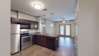 This single-floor residence offers a thoughtfully designed layout that combines comfort and modern style. The open-concept kitchen and living area serves as the heart of the home, featuring rich dark-wood cabinetry, granite countertops, and a peninsula island with a built-in sink and dishwasher. Stainless steel appliances — including a range, microwave, and refrigerator — complete the kitchen. Sleek pendant lights hang above the island, while hardwood-style flooring flows throughout the main living spaces, adding warmth and continuity. The living area is bathed in natural light from a set of French doors that open to the outdoors, and a ceiling fan overhead adds comfort. Two well-sized bedrooms feature plush carpeting, ceiling fans, and large windows that allow for generous natural light. The primary bathroom is appointed with a double-sink granite vanity, dark wood cabinetry, a soaking tub, and access to a spacious walk-in closet with built-in shelving. A secondary bathroom mirrors the same quality finishes, featuring a granite vanity and a tub-shower combination. Crown molding details and a consistent neutral color palette throughout give the space a polished, cohesive aesthetic.