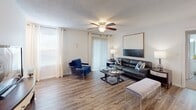 Located at 1011 W Butler Rd in Mauldin, SC, this single-floor residence offers a well-designed layout that balances comfort and functionality. The living area is bright and open, featuring wood-style flooring, a ceiling fan, and large windows alongside a sliding glass door that invites abundant natural light and outdoor access. The kitchen is efficiently laid out with white cabinetry, granite-style countertops, black appliances including an electric range and refrigerator, and matching wood-style flooring that ties the space together seamlessly. The unit includes two bedrooms, each carpeted and equipped with ceiling fans. The primary bedroom features a walk-in closet, while both rooms offer a comfortable, well-proportioned feel with ample window space for natural light. Two bathrooms serve the residence, each finished with wood-style flooring, white vanity cabinetry, and granite countertops. One bathroom features a wide vanity with an extended mirror, while both include a tub-shower combination. The overall aesthetic throughout the home is clean and contemporary, with neutral wall tones and consistent finishes that create a cohesive and inviting atmosphere across all rooms.