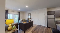 This single-story residence on Mulberry Blvd in Port Wentworth, Georgia offers a thoughtfully designed layout with modern finishes throughout. The entryway opens adjacent to a well-equipped kitchen featuring dark espresso cabinetry, granite countertops, stainless steel appliances including a refrigerator, range, and microwave, along with under-cabinet lighting and rich hardwood-style flooring. Crown molding accents the ceilings throughout the main living areas, adding a refined architectural detail. The spacious living room is bathed in natural light from large windows and glass doors, creating a bright and welcoming atmosphere. Recessed lighting complements the natural light, while the hardwood-style flooring transitions to plush carpet in the bedroom areas. The bedrooms offer generous proportions, large windows with ample natural light, and access to closet space. The bathrooms are finished with dark-toned vanity cabinetry, white countertops, framed mirrors, and tub/shower combinations. Neutral wall tones throughout the home provide a versatile backdrop, while the overall design balances comfort and contemporary style in a cohesive, move-in-ready package.